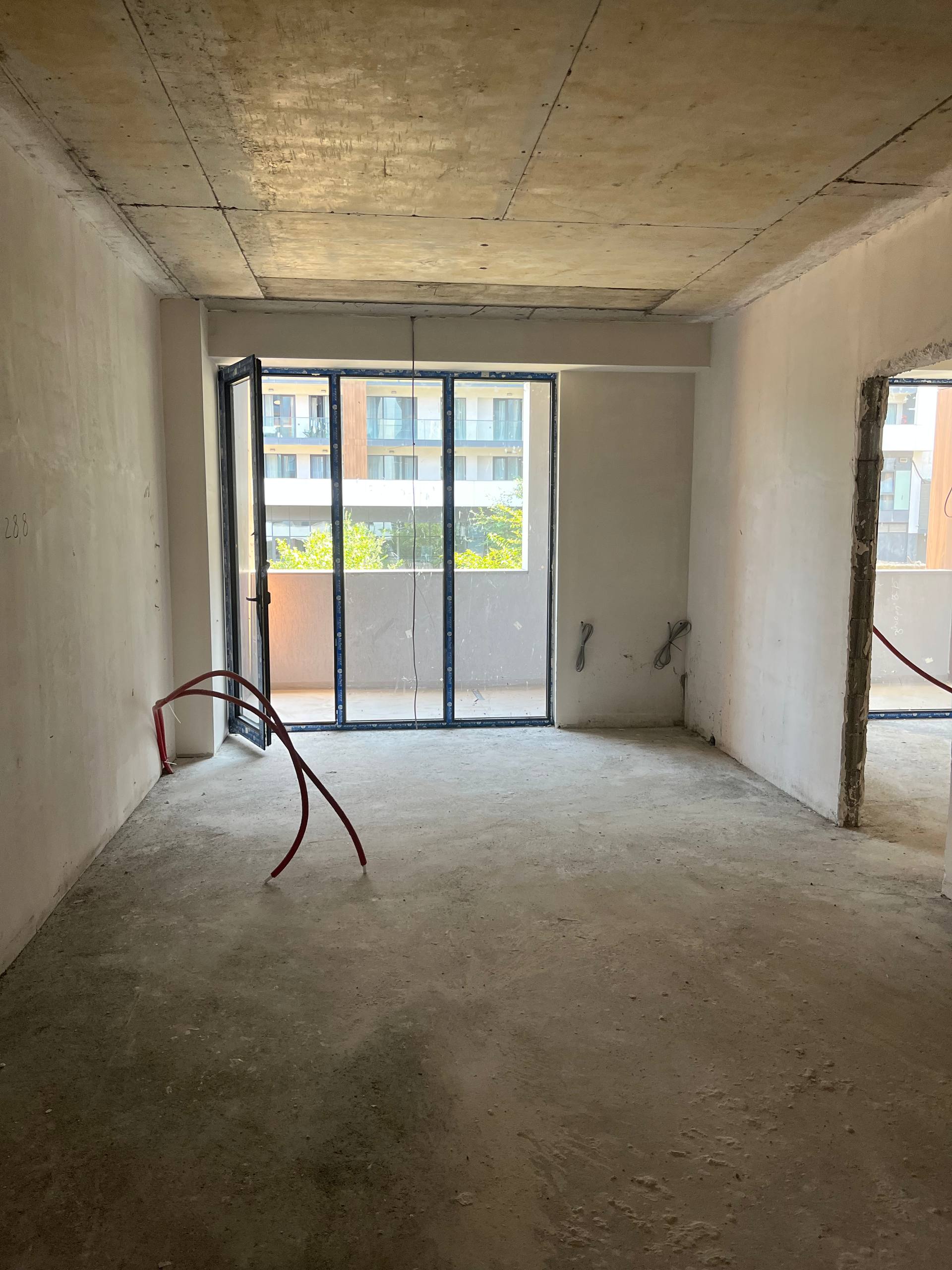Bare living room with raw concrete slab ceiling, plastered walls, unfinished concrete floor and installed balcony glazing