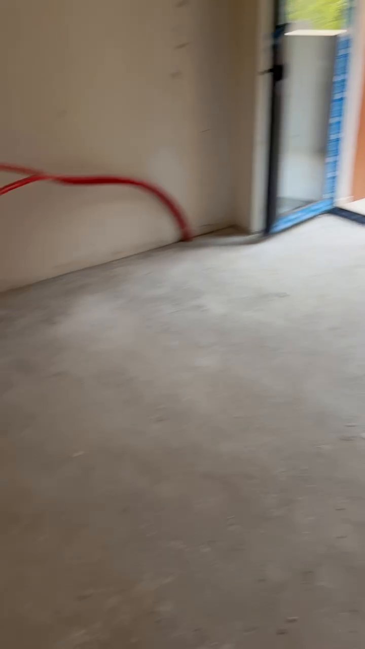 Living room floor with red PEX pipe runs lying loose on raw concrete