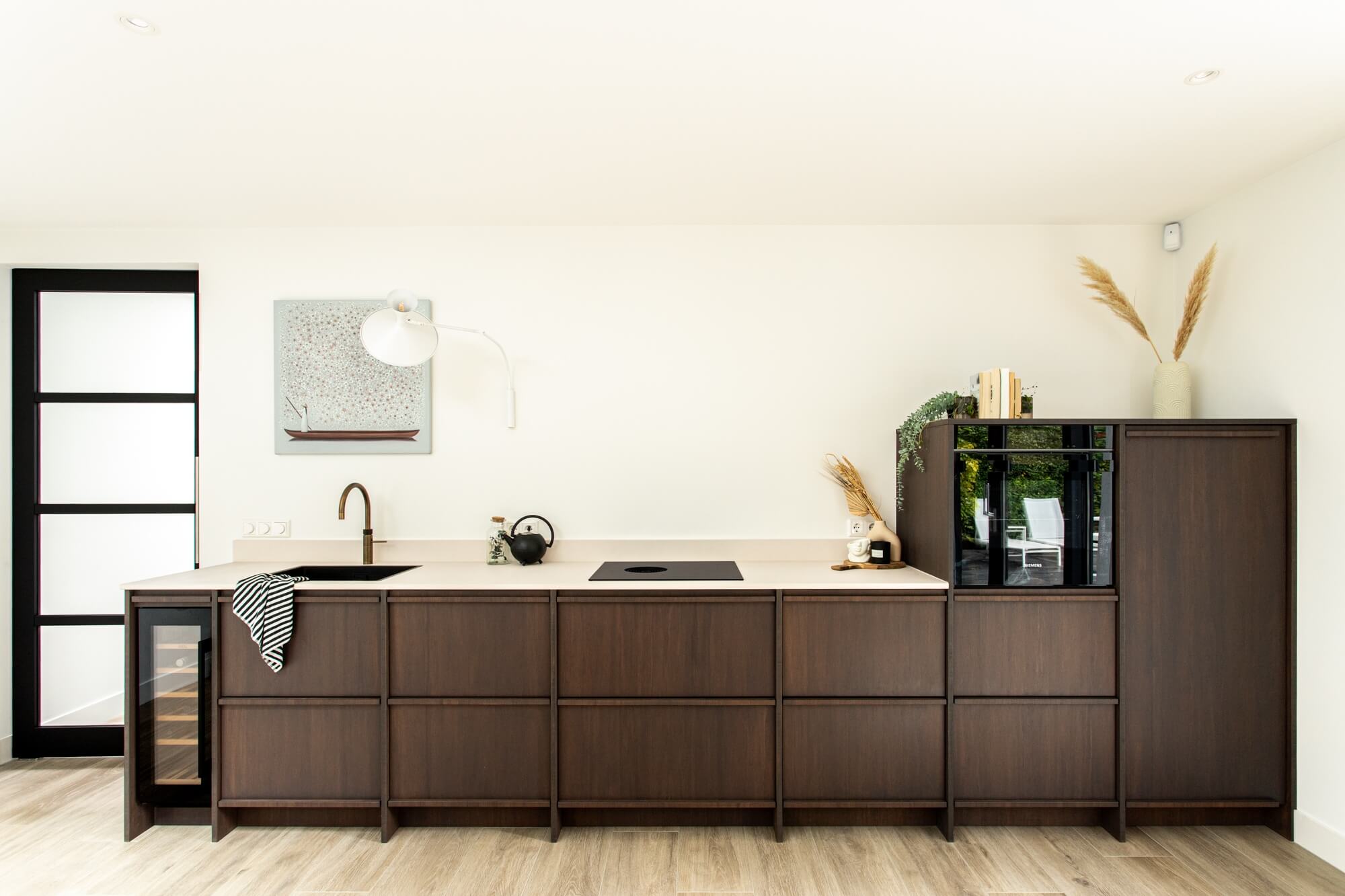 Handleless dark-stained oak kitchen run against a white wall with a pale stone worktop
