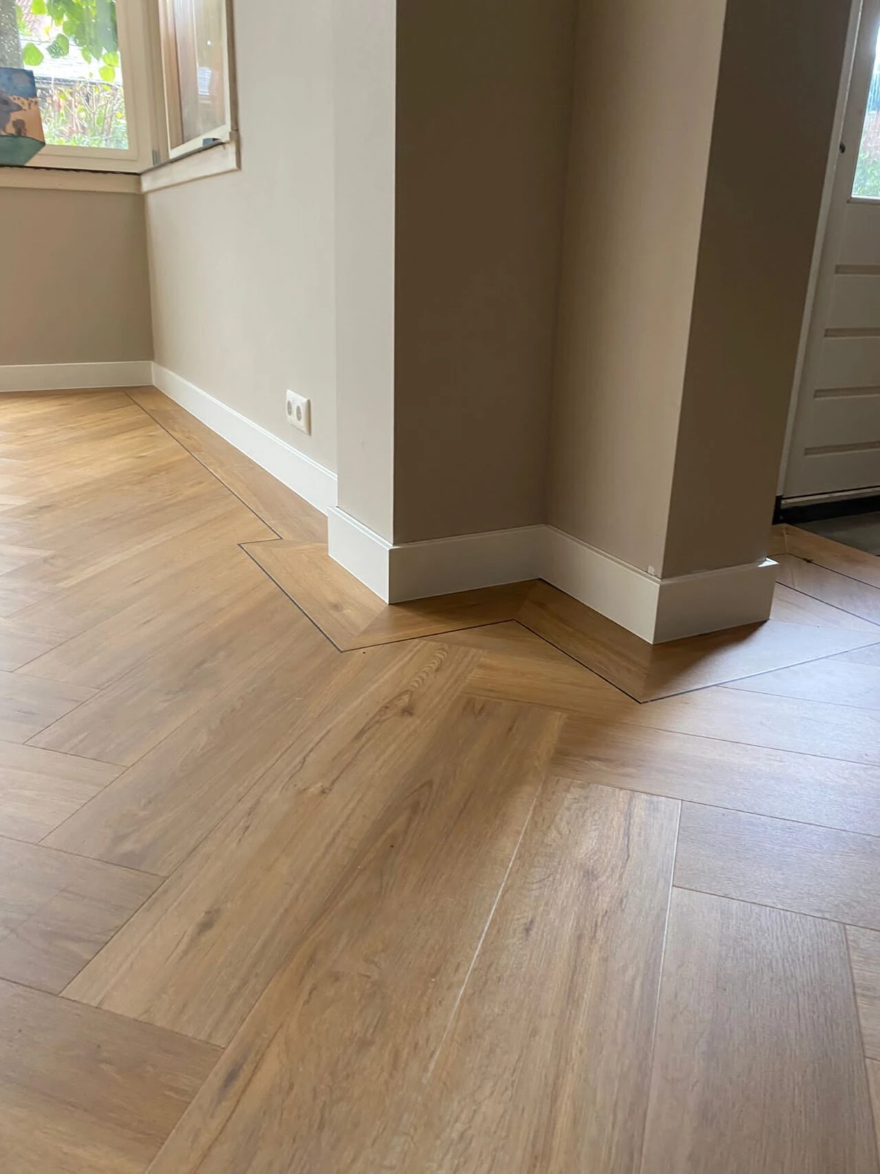 Wide herringbone oak-look floor meeting tall white skirting at a corner