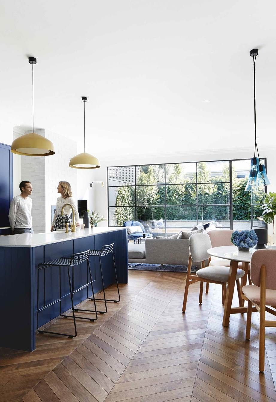 Navy kitchen island with a brass tap, brass pendant lights and a chevron wood floor