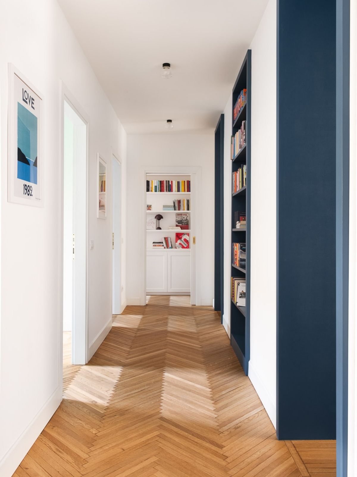 Hallway with navy built-in bookcase and wall, white doors and chevron oak floor